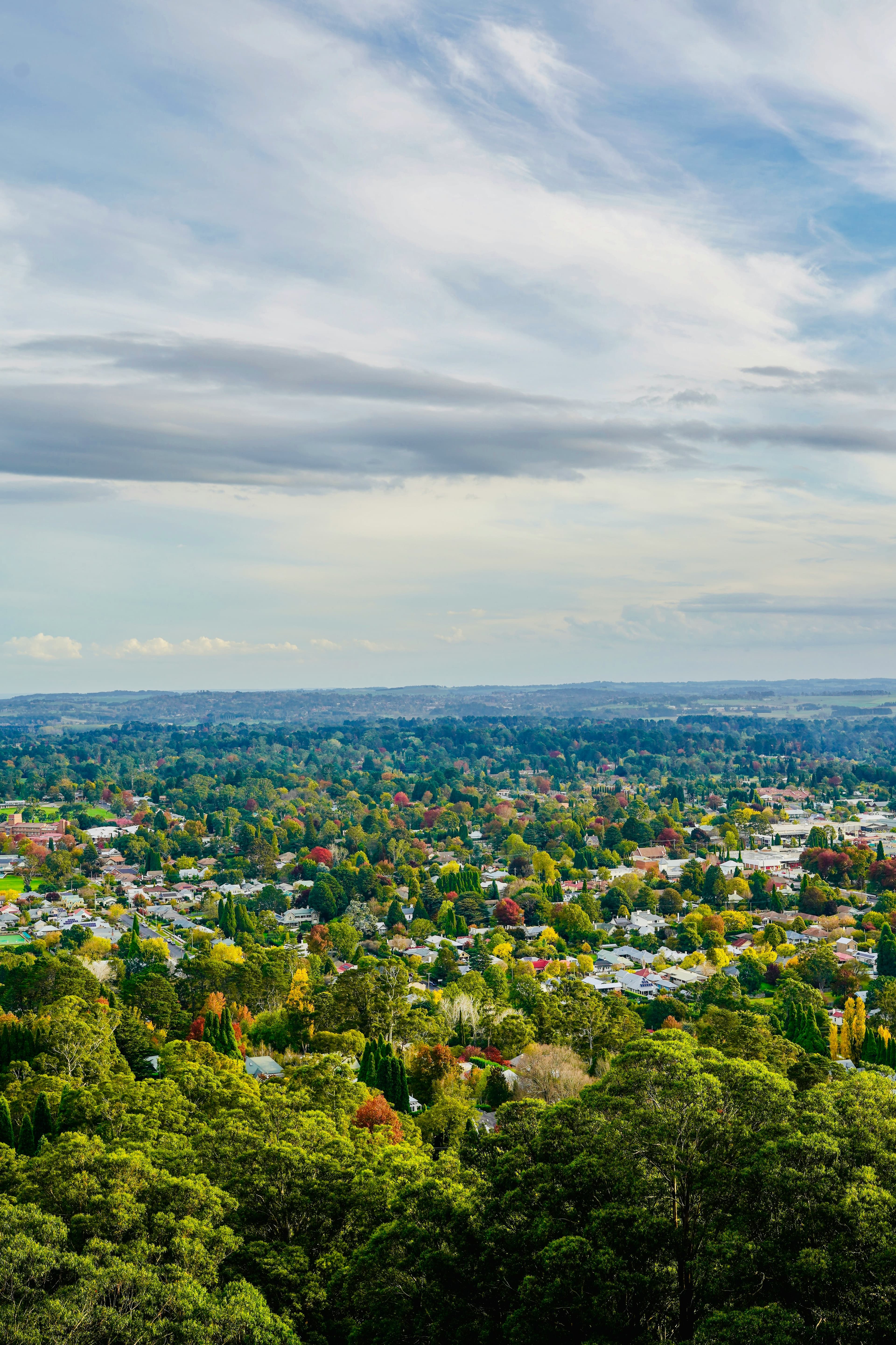 Aerial view of a town nestled in colorful autumn trees under a cloudy sky.